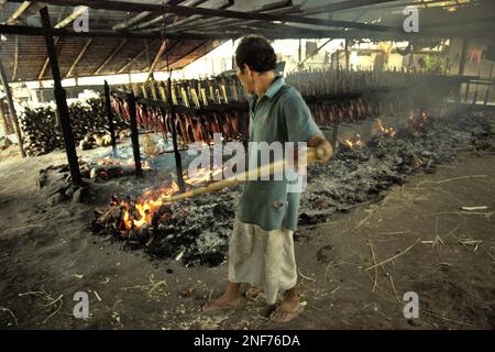 Un lavoratore sta mantenendo la distribuzione di buccia di cocco che brucia che è usato come combustibile per fumare le carni di tonno di skipjack ad un'industria domestica in Bitung, Sulawesi del nord, Indonesia. Popolarmente conosciuto come 'cakalang fufu', il tonno affumicato è considerato un 'cibo indigeno esotico', una parte della produzione di tonno di skipjack che è una delle attività economiche più importanti nella zona di Bitung City, uno degli anelli esterni dell'Indonesia di porti di pesca collegati all'Oceano Pacifico. Secondo la FAO nel loro ultimo rapporto chiamato Stato della pesca e dell'acquacoltura mondiale 2022, l'Indonesia è il terzo più grande... Foto Stock