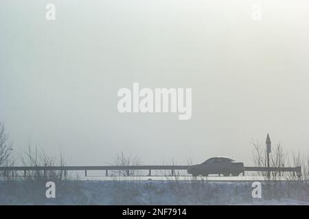 Auto passeggeri nella nebbia su una strada invernale con grandi nevicate sul lato della strada. Foto Stock