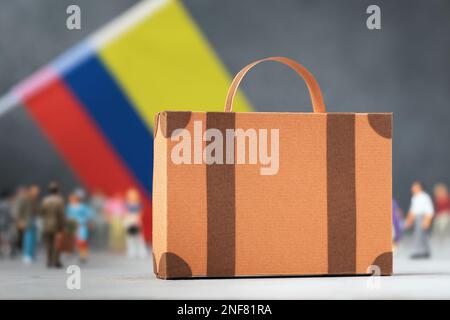 Valigia di cartone, personaggi di giocattoli di plastica e la bandiera colombiana su uno sfondo astratto, un concetto sul tema del trasferimento o della migrazione in Colombia Foto Stock