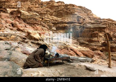 Aufstieg zum Kloster ad-Deir, Frau beim Teekochen an einem einsamen Lagerfeuer in der felsigen, verlassenen Stadt Petra, al-Batra, Hauptstadt des Köni Foto Stock