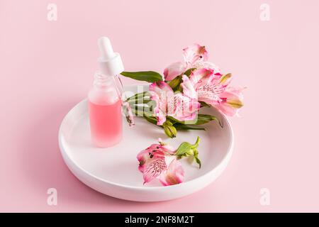 un flacone bianco opaco aperto con una pipetta riempita di crema idratante naturale per la cura della pelle si trova su una piastra in ceramica bianca. sfondo rosa Foto Stock