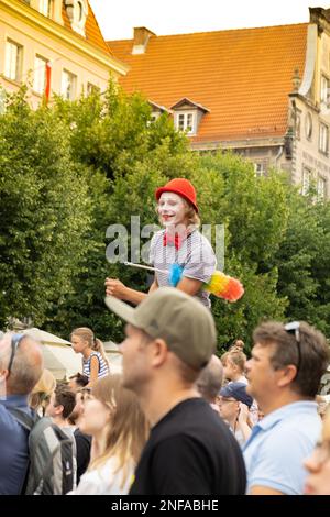 Gdansk, Polonia - 9 agosto 2022 Ritratto di clown fresco in parrucca luminosa. Parata durante la Fiera di Dominic a Danzica. Festival di intrattenimento in strada palafitte camminatore uomo in rosso giocoleria sorridente. Spettacolo teatrale per bambini al Foto Stock