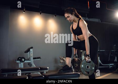 Donna sportiva che si esercita con il piatto del peso in palestra. Foto Stock