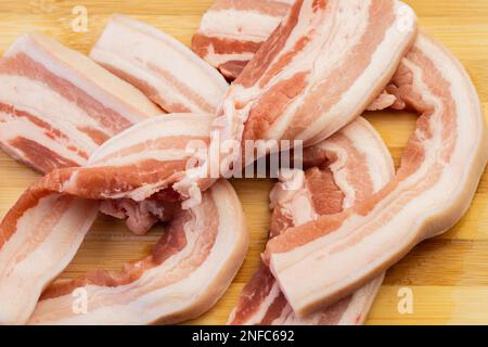 Un primo piano di strisce di pancetta posate su un tagliere di legno su una superficie di un tavolo Foto Stock