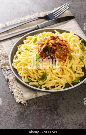 Tagliatelle di formaggio tirolese o pasta chiamata Kaespaetzle con cipolla fritta closeup sul piatto sul tavolo. Verticale Foto Stock