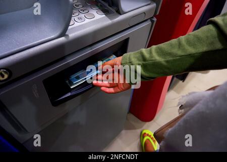 La mano di una donna sta ritirando denaro da una macchina ATM, in Una città di Muntok di notte Foto Stock