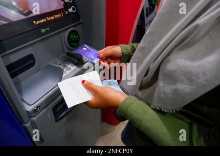 La mano di una donna asiatica che inserisce Una carta in una macchina ATM, a Muntok, Indonesia Foto Stock