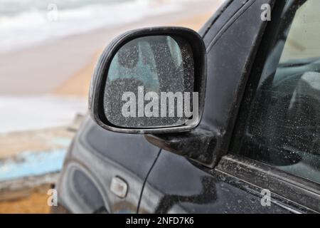 L'auto sporca ha bisogno di un lavaggio. Piccola vettura nera con sporcizia sullo specchietto laterale. Foto Stock