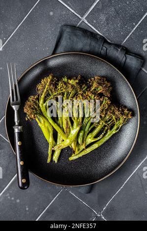 Broccolini verdi arrostiti con burro all'aglio in un piatto. Sfondo nero. Vista dall'alto. Foto Stock