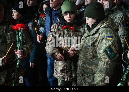 KHARKIV, UCRAINA - 16 FEBBRAIO 2023 - Servicewomen condividere la fiamma di una candela durante la cerimonia funeraria di Euromaidan attivista, vice ospedale co Foto Stock