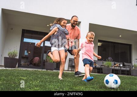 Padre e i suoi due figli corrono dopo un calcio che si abbassa sulla collina Foto Stock