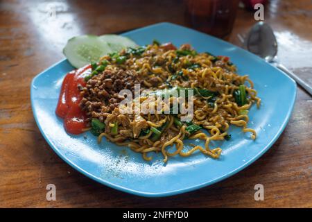 Indonesiano popolare Instant Noodle fritto. Servito con uova strapazzate, pomodoro, cetriolo, lattuga e peperoncino Foto Stock