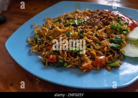 Indonesiano popolare Instant Noodle fritto. Servito con uova strapazzate, pomodoro, cetriolo, lattuga e peperoncino Foto Stock