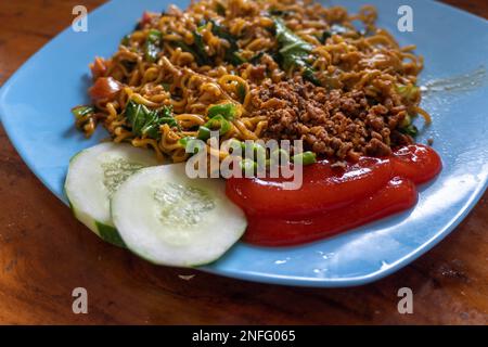 Indonesiano popolare Instant Noodle fritto. Servito con uova strapazzate, pomodoro, cetriolo, lattuga e peperoncino Foto Stock