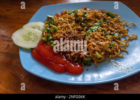 Indonesiano popolare Instant Noodle fritto. Servito con uova strapazzate, pomodoro, cetriolo, lattuga e peperoncino Foto Stock