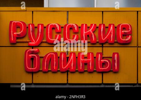 Primo piano su una luce al neon rossa a forma di breve frase russa 'русские блины' che significa 'frittelle russe' in inglese. Foto Stock