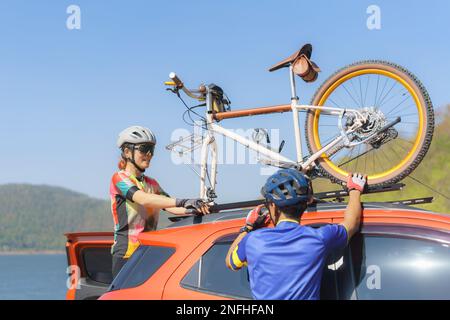 Coppia di ciclista asiatici che scaricano le biciclette dal tetto della loro auto in preparazione per un giro mattutino in bicicletta sul lago. Foto Stock