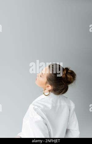 modello giovane in camicia bianca e orecchini a cerchio in posa isolata su grigio con spazio copia, immagine stock Foto Stock