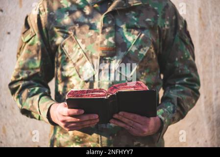 Soldato vestito in uniforme mimetizzata tenendo in mano una bibbia. Soldato che legge e medita sulla parola di Dio Foto Stock