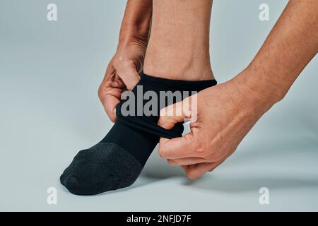 primo piano di un uomo che si mette su una calza a compressione, su uno sfondo bianco Foto Stock