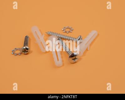 Viti e tasselli in plastica su sfondo arancione. Bulloni e perni di riferimento. Foto Stock
