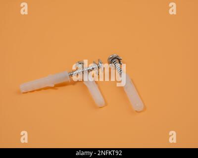 Viti e tasselli in plastica su sfondo arancione. Bulloni e perni di riferimento. Foto Stock