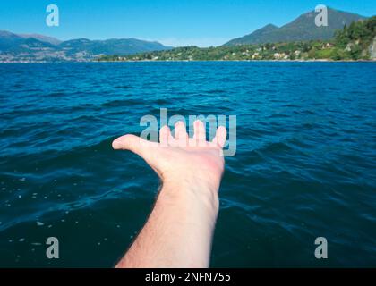 Il braccio maschile si allunga verso l'acqua, il lago maggiore, il Piemonte, l'Italia Foto Stock