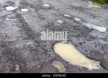 Buche sulla superficie stradale che rompono l'asfalto a causa del gelo invernale e del ghiaccio Foto Stock