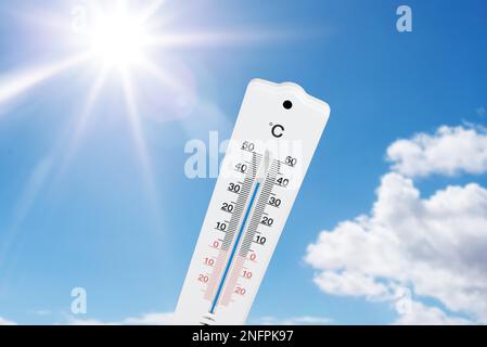 termometro per esterni che indica temperature elevate contro il cielo e il sole blu estivo Foto Stock