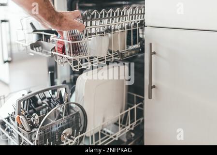 Close-up di uomo di carico o lo svuotamento di lavastoviglie in cucina Foto Stock