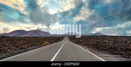 Vista panoramica di una lunga e diritta strada vuota attraverso il paesaggio vulcanico di Lanzarote, Isole Canarie Foto Stock