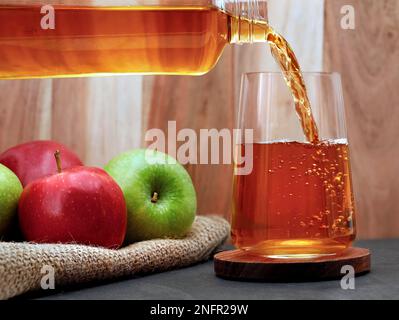 Il succo di mela fresco si versa da una bottiglia in un bicchiere sul tavolo, rinfrescante succo di frutta Foto Stock