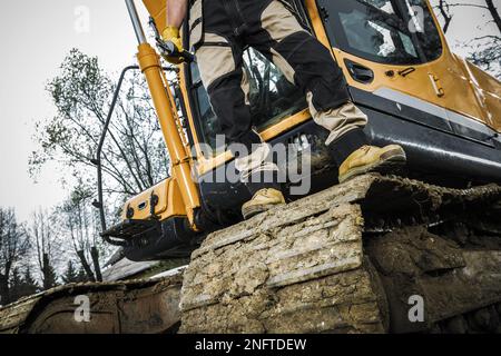 Operatore dell'escavatore industriale in piedi sul cingolo. Tema macchine da costruzione per impieghi pesanti. Foto Stock