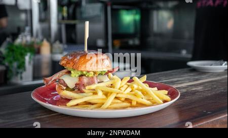 Un'immagine di un hamburger di manzo con pancetta appena grigliata servito con patatine fritte Foto Stock