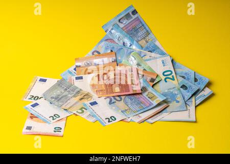 Sul tavolo c'è un mucchio di banconote in tagli da cinque, dieci, venti, cinquanta e duecento euro. Banconote miste in euro su sfondo giallo. Foto Stock