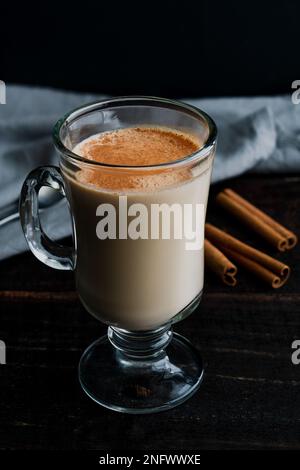 Accogliente tè Almond Rooibos latte con cannella: Una tazza di vetro riempita con un latte di tè e guarnita con cannella cosparsa Foto Stock