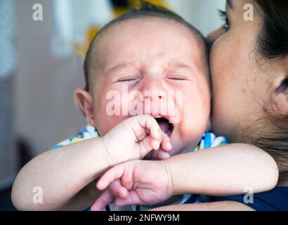 ritratto di un neonato sulla spalla di sua madre. Un neonato piange tra le braccia della madre Foto Stock