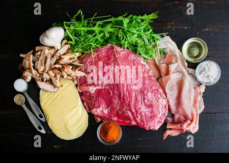 Bistecca farcita con prosciutto e funghi ingredienti: Bistecca cruda, funghi, formaggio e altri ingredienti su un tavolo di legno Foto Stock