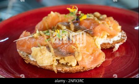 un'immagine ravvicinata di salmone affumicato e uova strapazzate su pane tostato guarnito con fiori commestibili Foto Stock