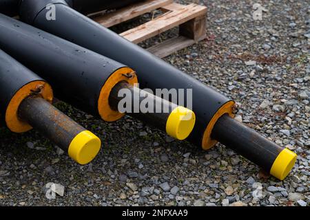 Tubi metallici neri in isolamento si trovano in un cantiere. Tappi di plastica gialli alle estremità dei tubi. Foto Stock