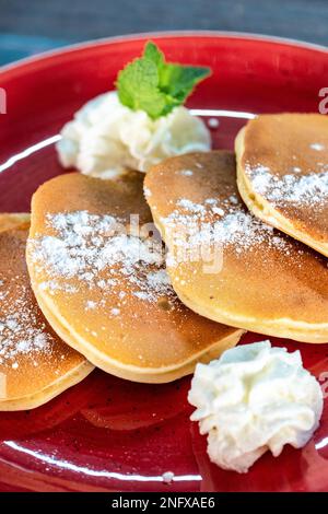 Un ritratto di primo piano di frittelle americane ricoperte di zucchero servite con panna montata Foto Stock