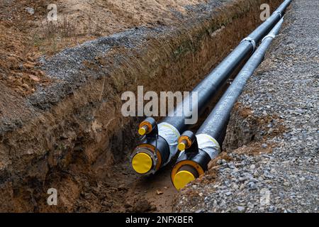 Grandi tubi metallici neri con guaina in plastica posta in una trincea. Moderna conduttura per la fornitura di acqua calda e riscaldamento ad un'area residenziale Foto Stock