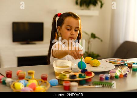 Carina bambina dipinge le uova con un pennello. Concetto di Pasqua. Foto Stock