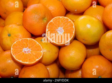 sfondo di molte clementine o tangerini arancioni mature e alcuni tagliati a metà Foto Stock