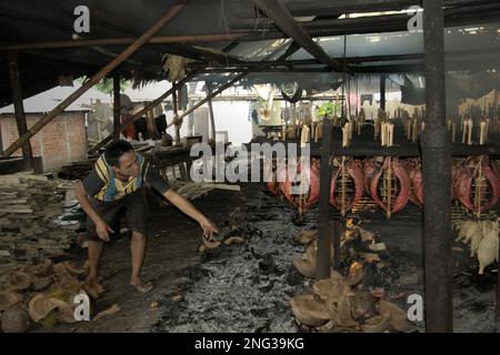 Un lavoratore sta mantenendo la distribuzione della combustione della buccia di cocco che viene utilizzata come combustibile per fumare le carni di tonno di skipjack, comunemente note come 'cakalang fufu', in un luogo di lavoro a Bitung, nel Nord Sulawesi, Indonesia. Secondo la FAO nel loro ultimo rapporto (2022), l'Indonesia è il terzo produttore mondiale di animali acquatici per la pesca e l'acquacoltura. Cinque paesi (Cina, India, Indonesia, Vietnam e Perù) sono responsabili di circa il 58% della produzione mondiale. L'Indonesia è anche uno dei paesi in cui gli alimenti acquatici contribuiscono per la metà o più all'assunzione totale di proteine animali. Foto Stock