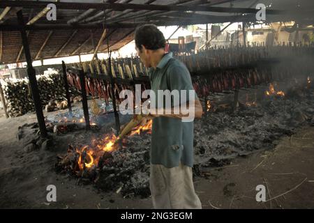 Un lavoratore sta mantenendo la distribuzione di buccia di cocco che brucia che è usato come combustibile per fumare le carni di tonno di skipjack ad un'industria domestica in Bitung, Sulawesi del nord, Indonesia. Secondo la FAO nel loro ultimo rapporto (2022), l'Indonesia è il terzo produttore mondiale di animali acquatici per la pesca e l'acquacoltura. Cinque paesi (Cina, India, Indonesia, Vietnam e Perù) sono responsabili di circa il 58% della produzione mondiale. Secondo la relazione, l'Indonesia è anche uno dei paesi in cui gli alimenti acquatici contribuiscono per la metà o più all'assunzione totale di proteine animali. Foto Stock