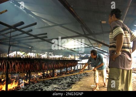 Un lavoratore sta mantenendo la distribuzione di buccia di cocco che brucia che è usato come combustibile per fumare le carni di tonno di skipjack ad un'industria domestica in Bitung, Sulawesi del nord, Indonesia. Secondo la FAO nel loro ultimo rapporto (2022), l'Indonesia è il terzo produttore mondiale di animali acquatici per la pesca e l'acquacoltura. Cinque paesi (Cina, India, Indonesia, Vietnam e Perù) sono responsabili di circa il 58% della produzione mondiale. Secondo la relazione, l'Indonesia è anche uno dei paesi in cui gli alimenti acquatici contribuiscono per la metà o più all'assunzione totale di proteine animali. Foto Stock