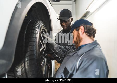 Immagine media di due meccanici che sostituiscono uno pneumatico. Concetto di reapir shop. Foto di alta qualità Foto Stock