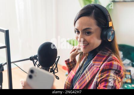 Podcaster femmina che registra video in interni per il pubblico su Internet utilizzando il suo smartphone. Foto di alta qualità Foto Stock