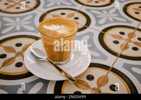 Bicchiere di caffè espresso appena preparato con latte cremoso su vetreria da tavolo a mosaico per cappuccino mocaccino americano con latte di cocco. CA Foto Stock